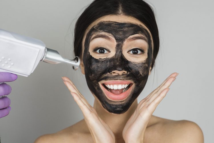 Asian woman with black mask on face with surprised emotionon, advertising procedure of carbon peel